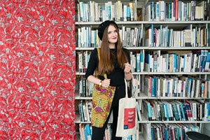 A young woman holding two canvas bags in front of a wall of books