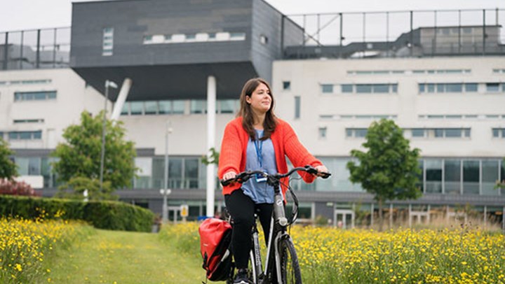A young woman cycling through the field outside the  University campus