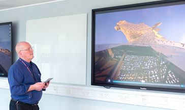 A 性用社 staff member standing by 2 screens showing the Scottish Kelpies sculpture