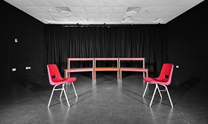 A dimly lit performance studio with two empty chairs centre stage, 