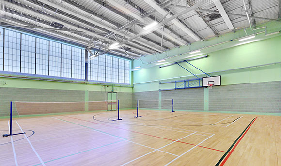 A large, bright sports hall with tennis nets, basketball nets and large windows