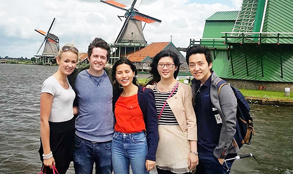 A row of smiling students posing for a photo by some windmills in Holland