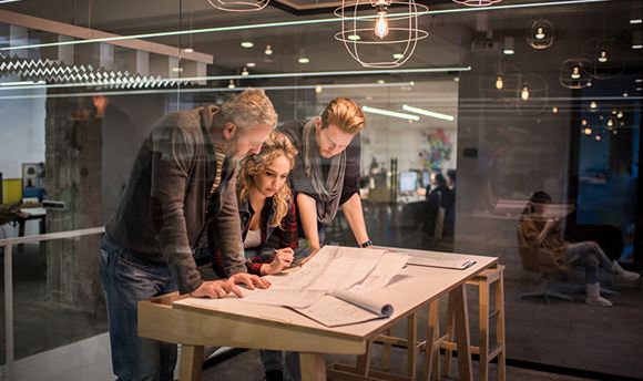 Three people gather around a desk looking at information
